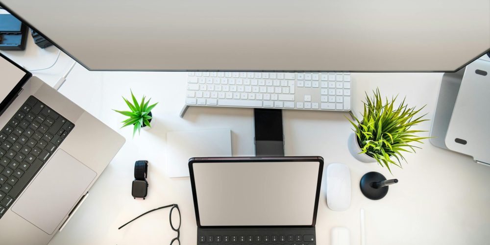 Top view of a minimalist workspace setup with laptop, tablet, and greenery.